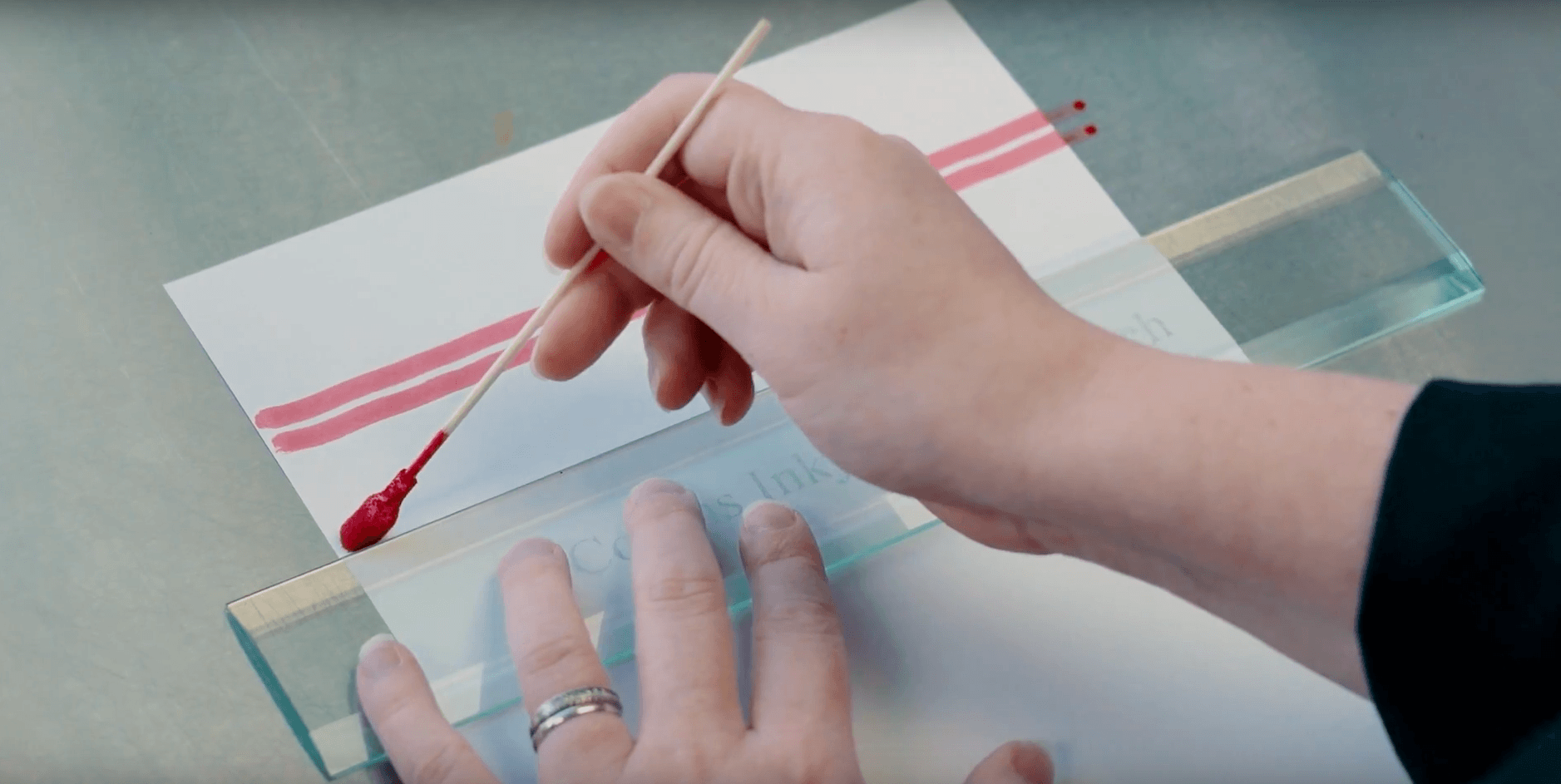 A person using a small tool to apply red ink lines on a sample for color matching or quality control testing.